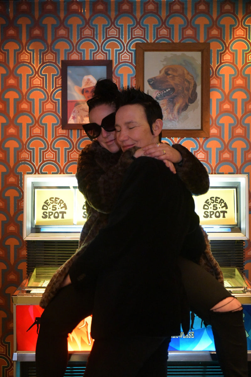 Two embracing ladies sitting on a jukebox in front of Londubh Studio's Enlightenment Panaeolus mushroom wallpaper in the entry way of Desert 5 Spot at the Tommy Hotel in Hollywood.