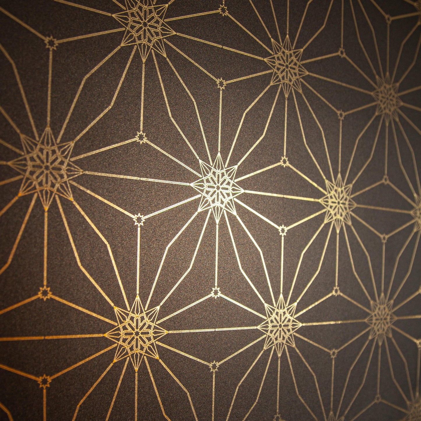 Star Guitar Night is a shimmering repeat moroccan inspired pattern and star motif linked together with a graphic thread in black digitally printed on gold mylar - shown at an angle with the light catching off the gold