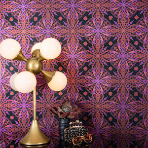 ChaCha Chill is a 1920s art deco inspired shimmering repeat geometric pattern composed of stars, diamonds, triangles, and other shapes in 70s retro pinks, reds, oranges, burgundy, on a black background and digitally printed on silver mylar - shown in a vignette with a deco lamp, a plant, vintage Ray Ban sunglasses and a black leather Alexander McQueen clutch bedazzled in skulls. 