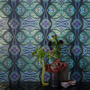 Ulu Canopy is a graphic repeat pattern featuring various organic motifs geometrically woven together in various greens and blues outlined in gold, digitally printed on gold mylar and shown in vignette with flowers in a vase.
