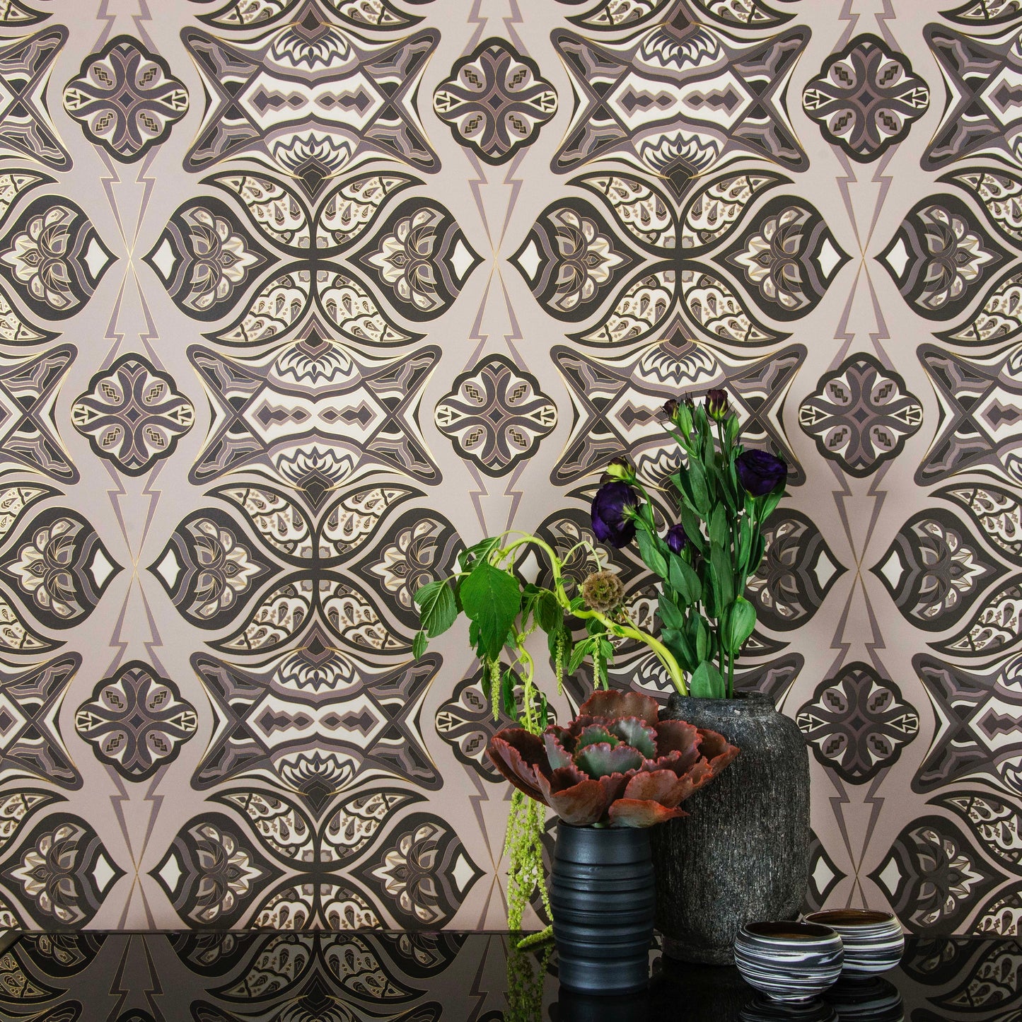 Ulu Dunes is a graphic repeat pattern featuring various gold outlined organic motifs geometrically woven together in various grays and warm whites outlined in gold, digitally printed on gold mylar and shown in a vignette with flowers in pottery vases