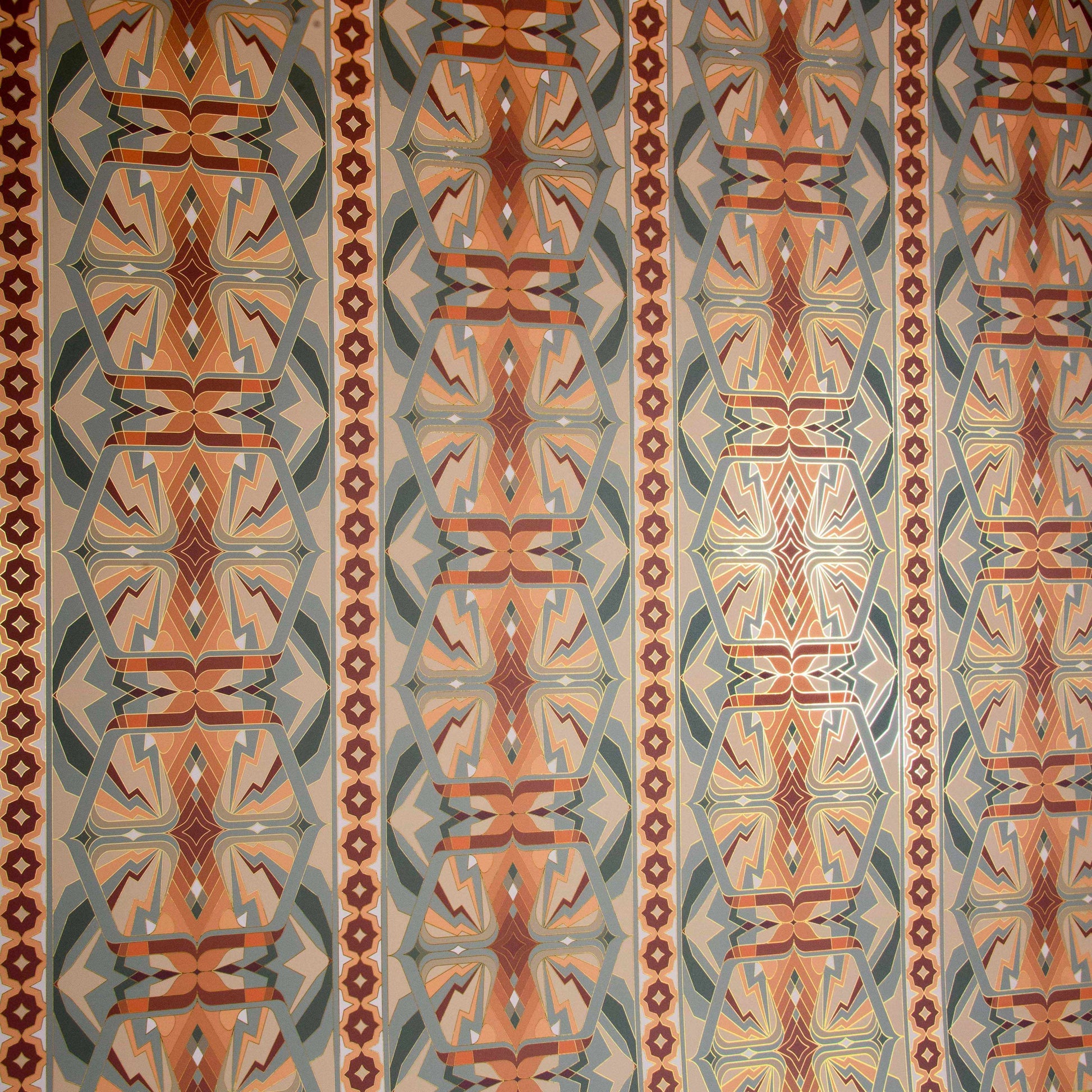 Sampa Terra is a riff of a classical vintage repeat linear geometric pattern wallpaper in earth tones, greens and oranges, with all shapes outlined in gold digitally printed on gold mylar shown at an angle with the light catching off the gold
