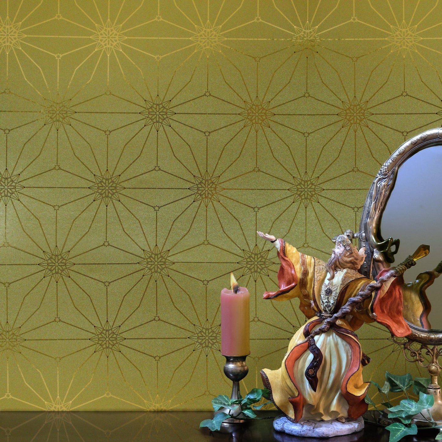 Star Guitar Dawn is a shimmering repeat moroccan inspired pattern and star motif linked together with a graphic thread in brass tone digitally printed on gold mylar - shown in a vignette with a candle and sculpture