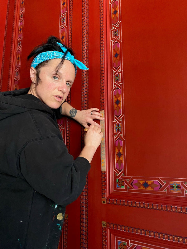 A cute artist stenciling a detailed pattern on doors