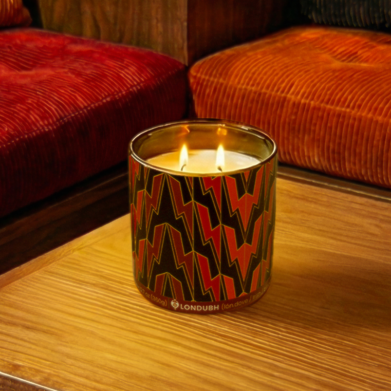 The Greased Lightning Candle, lit with two wicks, sits on a wooden table in a warmly lit room.