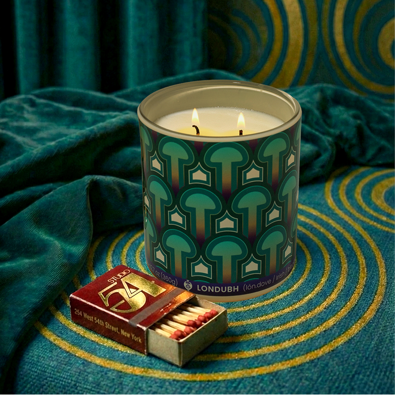 The Enlightenment Candle glows on a teal stool next to an open matchbox, with velvet drapes behind.