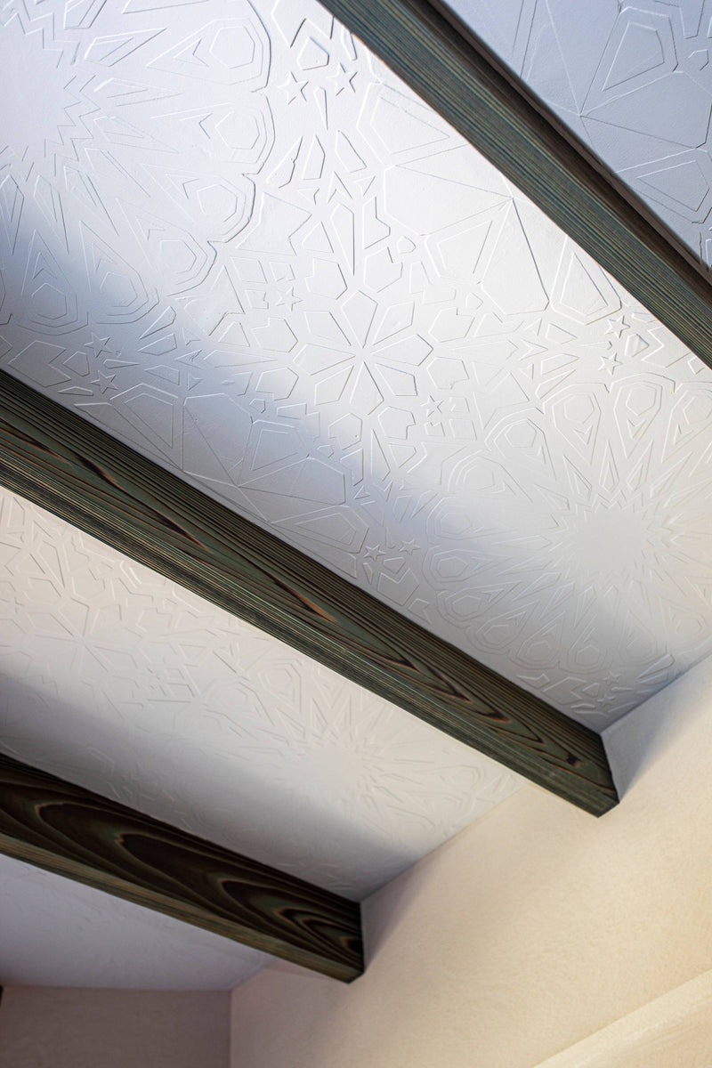 A custom textured white ceiling with a Moroccan geometric star pattern between dark wood beams.
