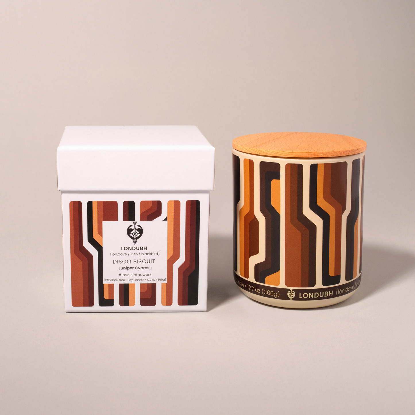 The Disco Biscuit Candle in a retro brown and orange pattern, positioned next to its matching gift box.