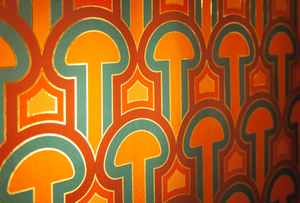 Enlightenment Panaeolus is a shimmering repeat geometric pattern featuring mushrooms and the portals of discovery they inspire, in orange, red, pink, blue, colors inspired by David Bowie's Aladdin Sane album cover, printed on gold mylar