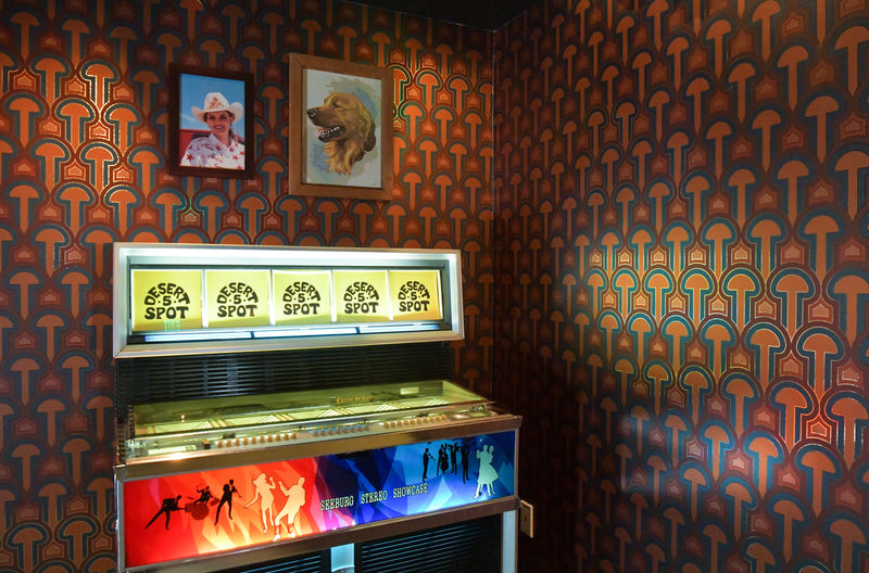 A vintage jukebox stands in a corner against the Enlightenment 'Panaeolus' Wallcovering.