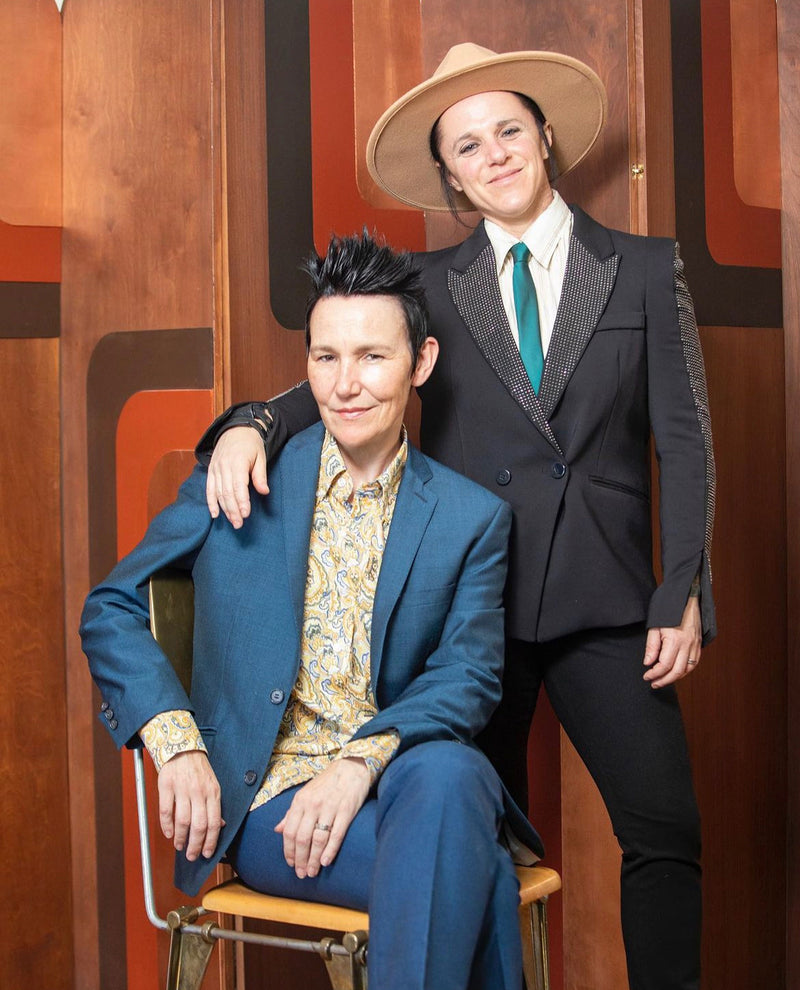 Founders Lisa Donohoe and Brynn Gelbard posing against a wood-paneled wall.