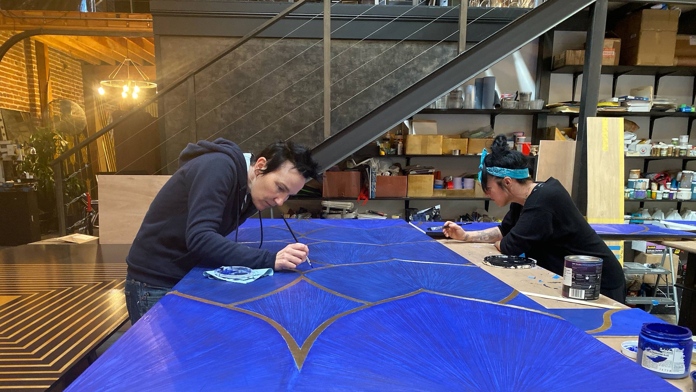 Founders Lisa Donohoe and Brynn Gelbard hand-painting a large custom cobalt blue and gold panel.