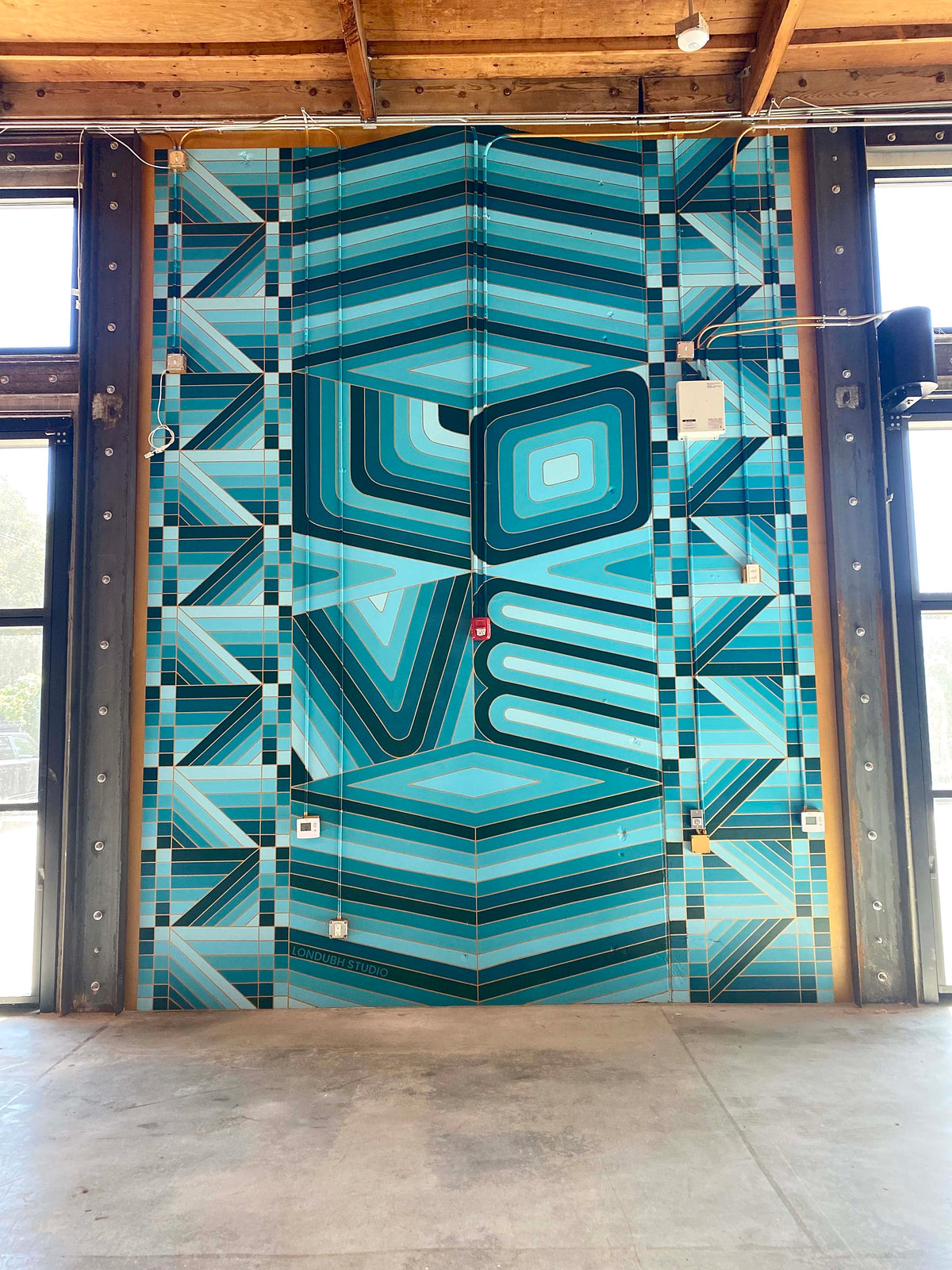 Hand-painted geometric ‘Love’ mural at TOMS Shoes Headquarters by Londubh Studio — large-scale wall art celebrating connection and color.