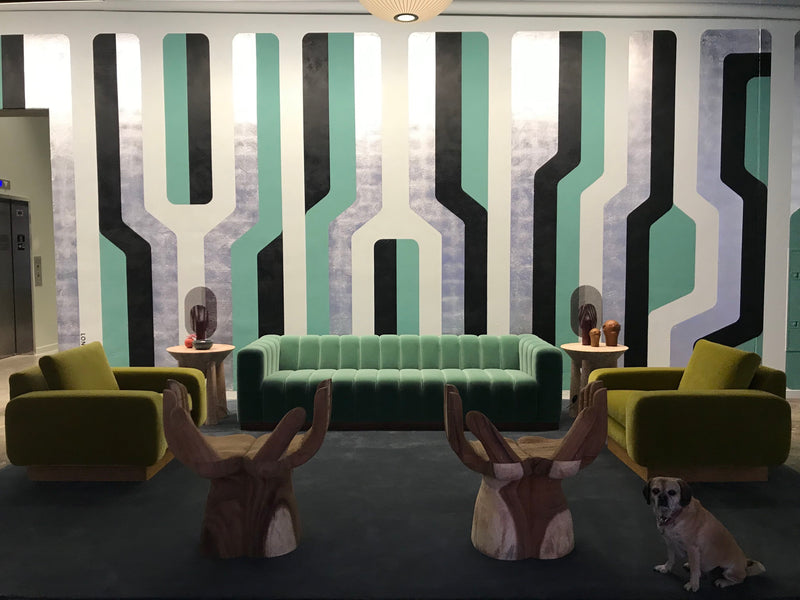 A furnished lobby with a large mural featuring teal, silver, and black stripes, and a green sofa.