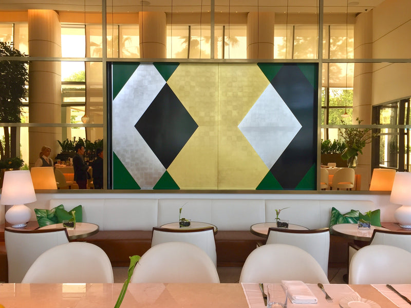 A large geometric art panel in gold, silver, black, and green hangs above a white banquette.