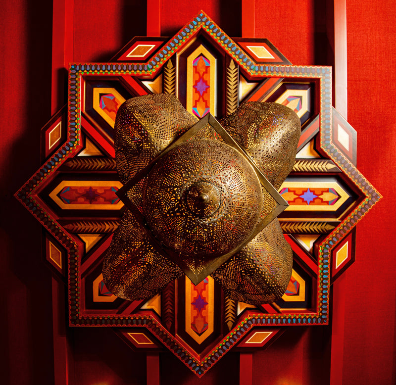 An ornate brass lantern hangs from a hand-painted, eight-pointed star medallion on a red ceiling.