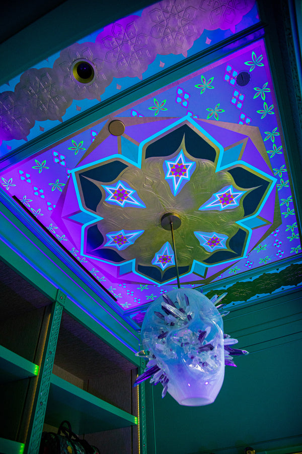 The central design appears twice across the ceiling. In each instance, it is comprised of four separate panels and features acrylic and fluorescent paints and textured plaster elements gilded in 22-carat gold leaf.