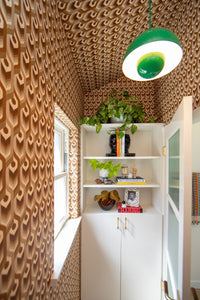 Wallpaper installation of custom grasscloth Neowise wallcovering shown on all four walls and ceiling of small powder room. is a maximalist retro repeat pattern wallpaper inspired by a comet that flew over Newgrange in Ireland and looks like a feather motif but is inspired by grain, and is 70s browns oranges, and gold, and printed on gold mylar.