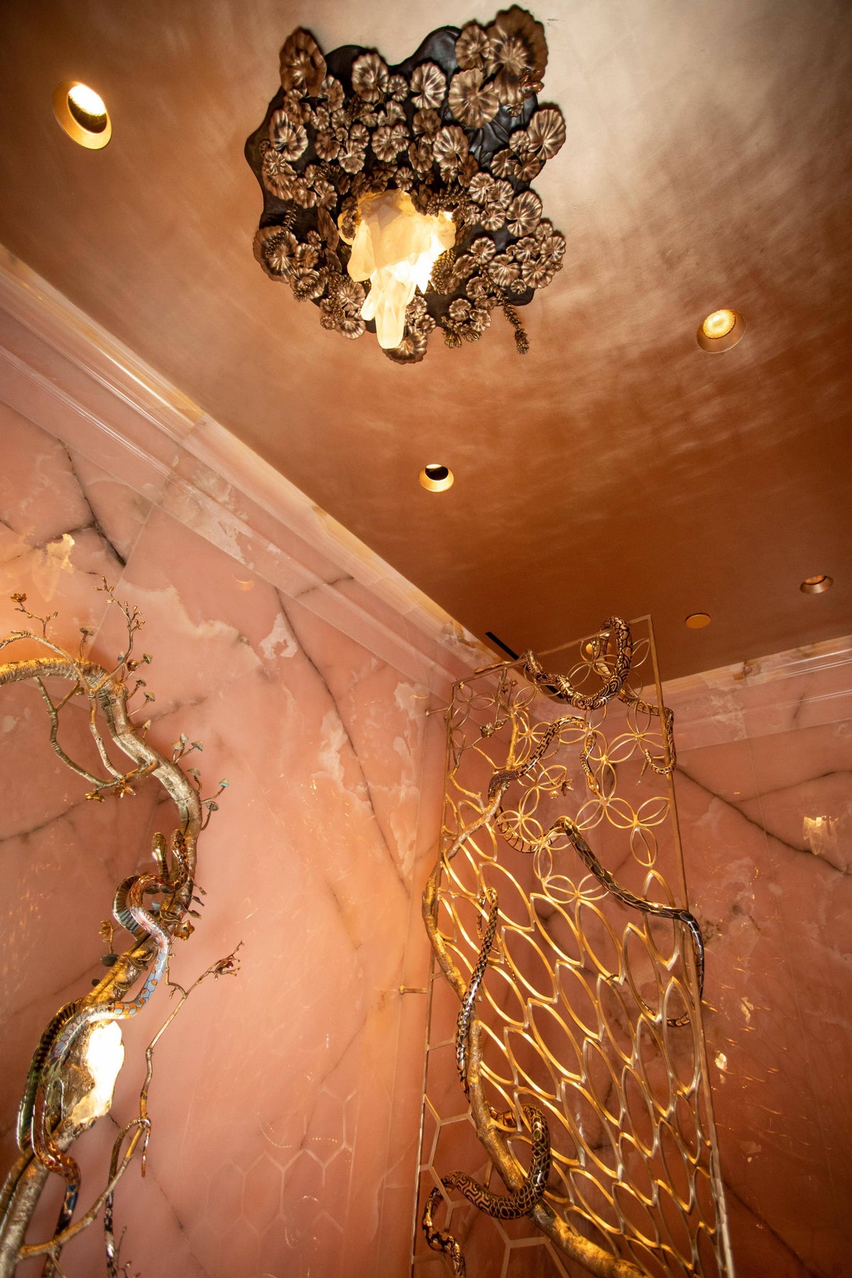 An opulent bathroom with pink onyx walls, a metallic ceiling, and a sculptural gold screen.
