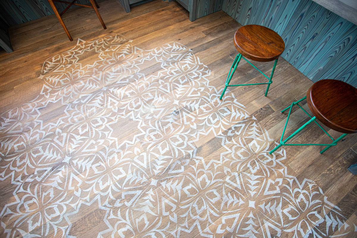 An intricate white pattern stenciled onto a wood floor, viewed from above with two stools.