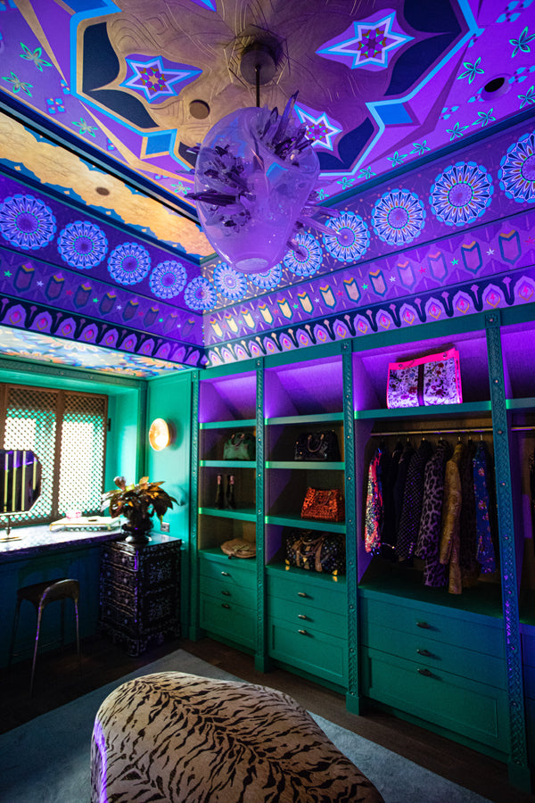 A maximalist walk-in closet with teal built-ins and a vibrant, custom ceiling under purple light.