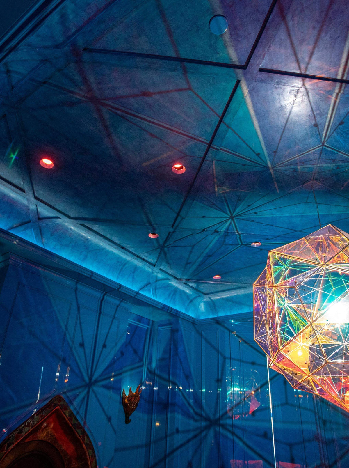 A room with a blue geometric ceiling and a large, glowing iridescent polyhedral light fixture.