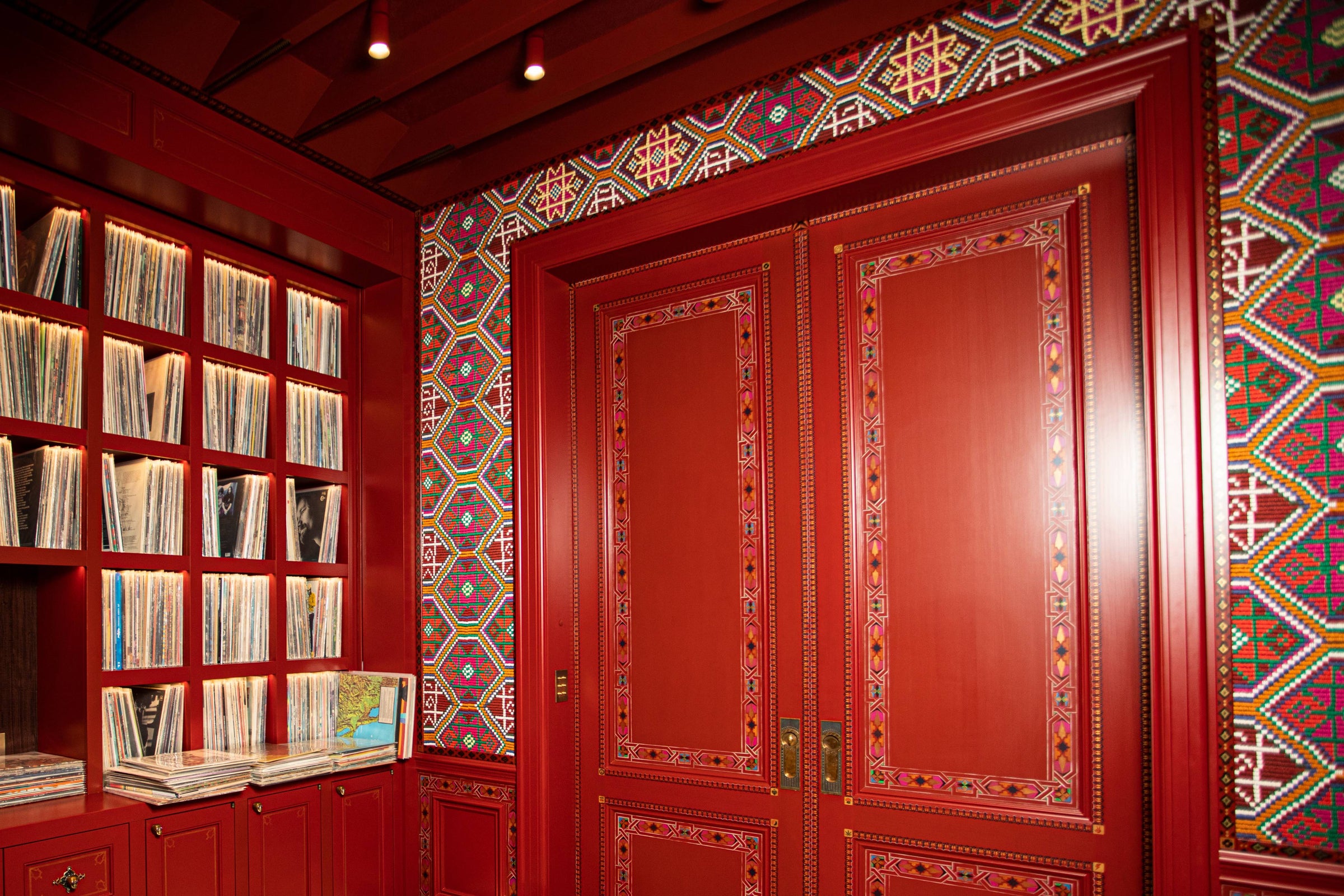 A listening room with custom red cabinetry, doors, and a colorful geometric wallcovering.