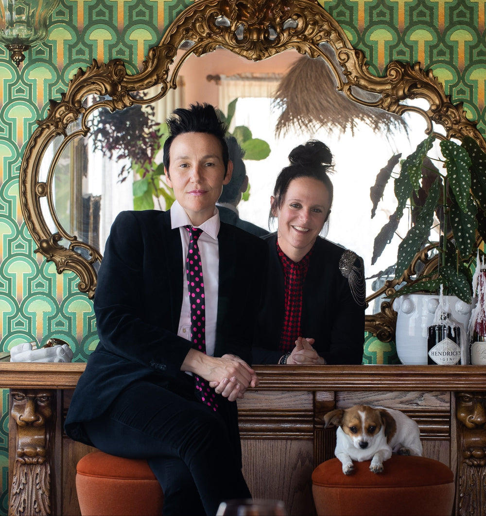 Two people sitting at a bar counter with a dog, in front of a decorative mirror and Londubh Studio's Enlightenment mushroom wallpaper.