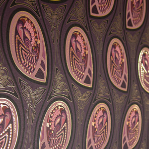 Peacock Nouveau Aubergine is a Celtic and Art Nouveau inspired maximalist repeat pattern wallpaper featuring peacocks and Celtic knot work in pinks, purples, all outlined in gold and digitally printed on gold mylar  - shown at an angle with the light catching off the gold