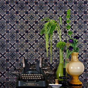 A repeating geometric pattern featuring four cannabis and marijuana leaves digital printed on gold mylar shown in vignette with typewriter and plant.