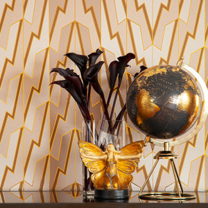 Greased Lightening Cream Dreams is a repeat art deco inspired gothamesque geometric pattern showcasing the lightning bolt, in neutral warm whites, beiges, and tans, outlined in gold and printed on gold mylar - shown here in a vignette with a little butterfly statue, black flowers and a vintage globe