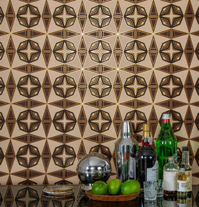 Integratronic Desert is a mid-century retro repeat geometric pattern featuring beiges and browns outlined in gold and digitally printed on gold mylar - shown in a vignette with a small bar set up with bottles, limes, a shaker, and shot glasses