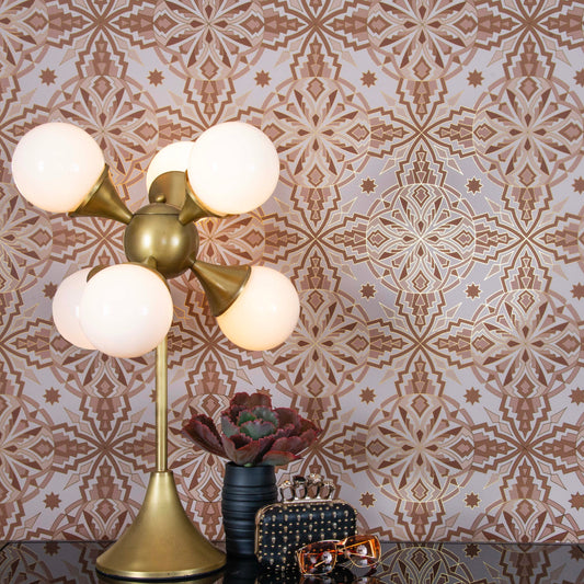 ChaCha Chill is a 1920s art deco inspired repeat geometric pattern composed of stars, diamonds, triangles, and other shapes in neutral tones outlined in gold on a warm white background and digitally printed on gold mylar - shown here in a vignette with a plant, a deco lamp, vintage ray ban sunglasses and a black leather Alexander McQueen clutch bedazzled in skulls.