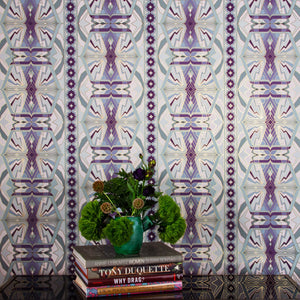 Sampa Orchid is a riff of a classical vintage repeat linear geometric pattern wallpaper in light purples, light greens, and whites, with all shapes outlined in gold digitally printed on gold mylar - shown here in a vignette with flowers and coffee table books. 